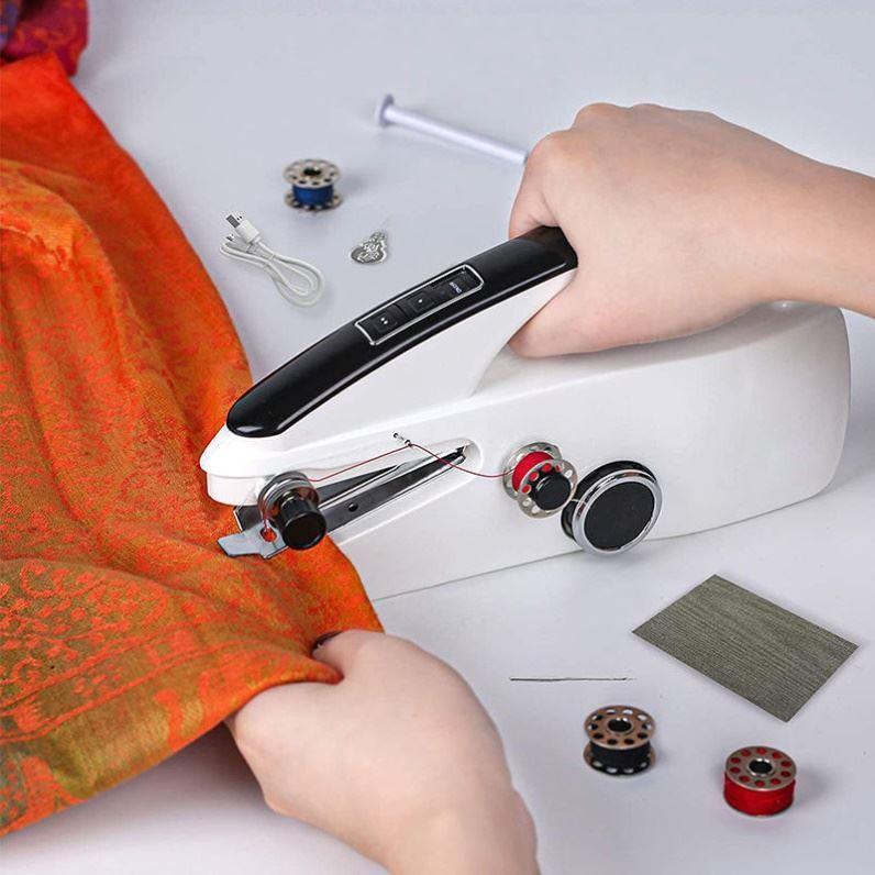 Handheld sewing machine being used on an orange fabric with various sewing accessories on a white background.